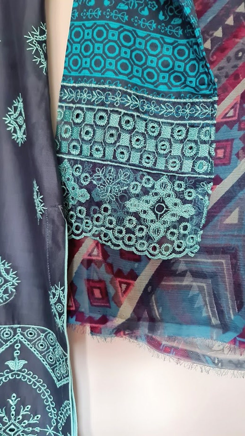 May include: A teal and black fabric with intricate embroidery. The fabric has a geometric pattern and a floral design. The fabric is trimmed with a lace border.