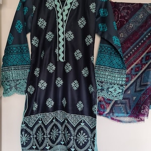 May include: A black and teal embroidered dress with a matching teal scarf. The dress has a scalloped neckline and sleeves, and the scarf has a geometric pattern.