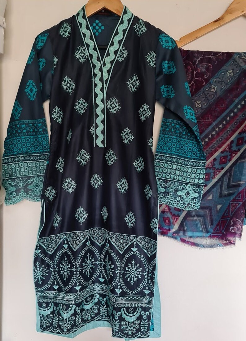 May include: A black and teal embroidered dress with a matching teal scarf. The dress has a scalloped neckline and sleeves, and the scarf has a geometric pattern.