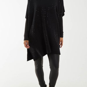 May include: A black knit poncho with a high neck and a subtle sparkle pattern. The poncho is worn with black leggings and black heeled ankle boots.