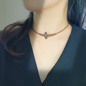 May include: A brown leather choker necklace with a green gemstone pendant. The pendant is set in a silver-toned metal frame.
