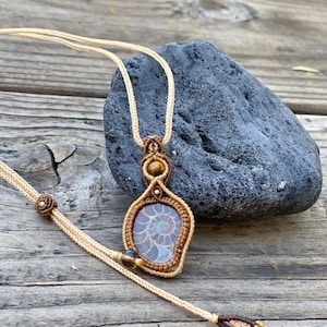 May include: A tan macrame cord necklace with a brown and white ammonite pendant and tiger's eye beads.
