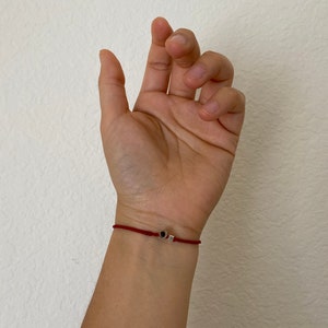 May include: A red string bracelet with a small silver charm featuring a black stone.