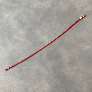 May include: A red braided cord with a white and brown bead at the end.