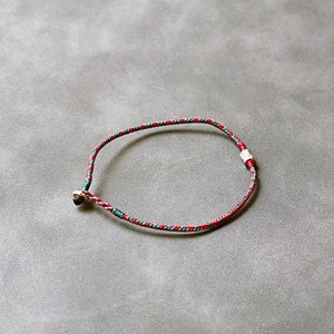 May include: A red and green braided bracelet with silver metal accents.