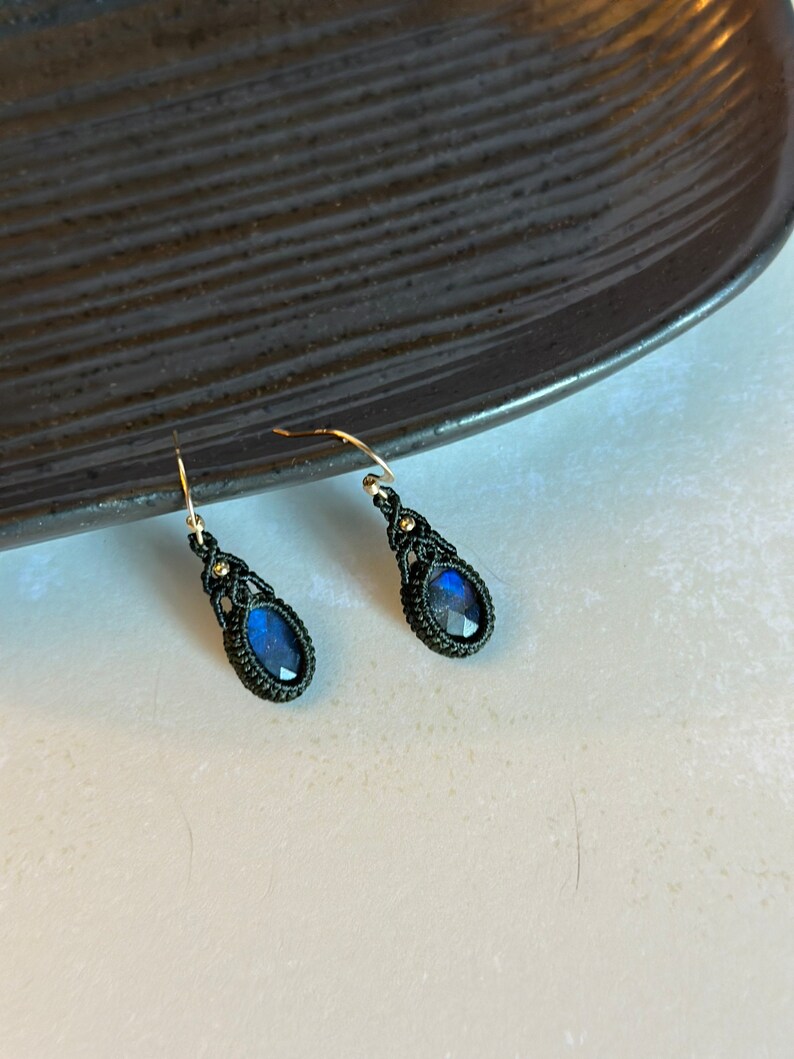 May include: A pair of dangle earrings with blue gemstone accents and black macrame detailing.