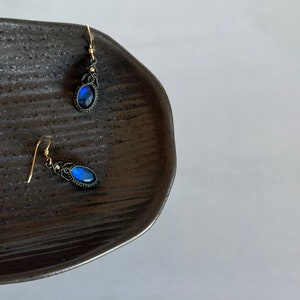 May include: A pair of blue gemstone earrings with black wire wrapped around the stone and gold hooks.