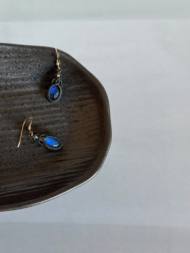 May include: A pair of blue gemstone earrings with black wire wrapped around the stone and gold hooks.