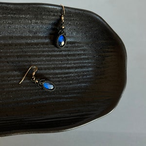 May include: A pair of blue gemstone earrings with black macrame detailing and gold hooks.