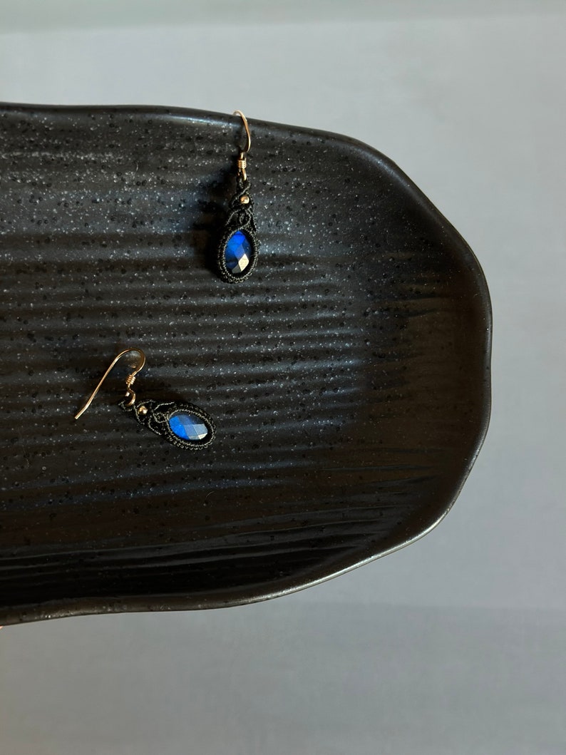 May include: A pair of blue gemstone earrings with black macrame detailing and gold hooks.