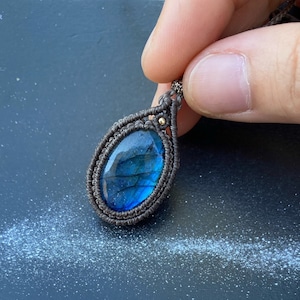 May include: A dark blue labradorite gemstone pendant with a silver-toned setting, wrapped in a dark gray cord.