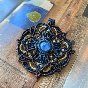 May include: A brown, blue, and gold macrame pendant with a blue iridescent gemstone in the center.