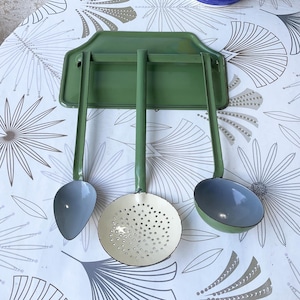 May include: A wall-mounted kitchen utensil rack in sage green with three matching hanging tools. The set includes a solid spoon, a perforated skimmer, and a deep ladle, all featuring long green handles and light-coloured interior bowls.