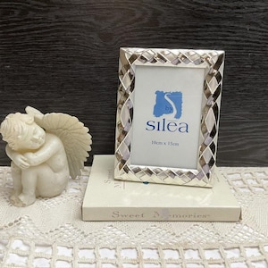 Può includere: Cornice per foto argentata con un design intrecciato e un passepartout bianco. La cornice misura 10 cm per 15 cm e ha il testo "by Silea" sul davanti.