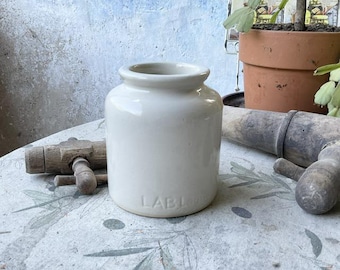 May include: A white ceramic jar with a rounded shape and a slightly flared top. The jar has a label that reads "LABI" on the front.