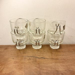 May include: Set of six clear glass cups with silver metal handles. The cups are stacked in pairs, with the handles facing outward.