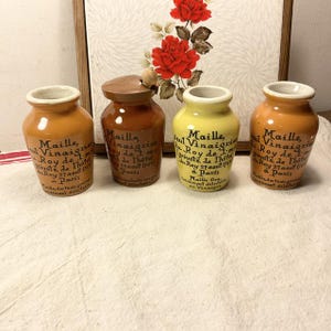 Può includere: Quattro bottiglie di ceramica vintage con tappi di sughero. Le bottiglie sono etichettate "Maille Vinaigrier du Roy de l'Hote" e sono decorate con lettere nere su uno sfondo giallo e marrone.