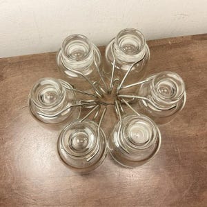 May include: A set of six clear glass cups with silver metal holders. The cups are arranged in a circle, with the holders connecting them together.