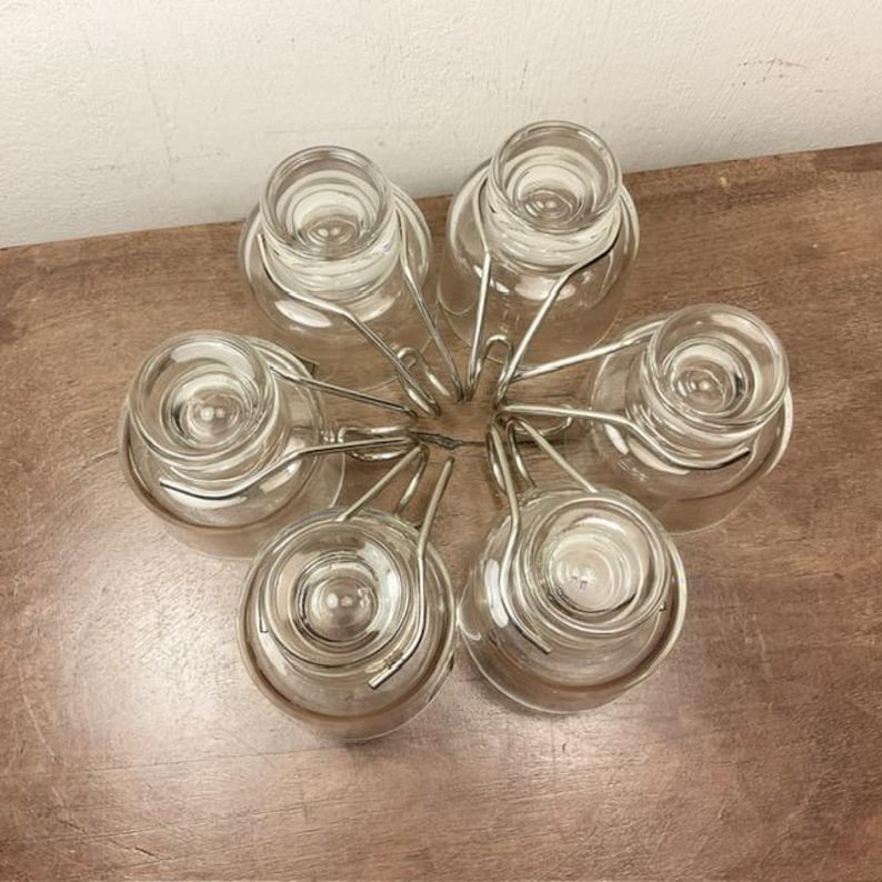 May include: A set of six clear glass cups with silver metal holders. The cups are arranged in a circle, with the holders connecting them together.