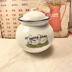 Peut inclure: Une boîte en céramique blanche avec un bord bleu et un couvercle. La boîte est décorée de trois canards blancs avec des nœuds bleus marchant sur un champ vert.