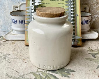 May include: A white ceramic jar with a cork lid. The jar has a label that reads "LAB Lagr".