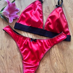 Women's red lingerie satin triangle bra and matching red thong lingerie set with satin black bows and adjustable straps sizes 28 - 38.