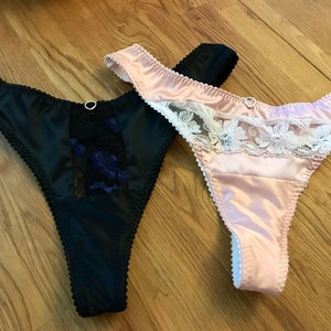 May include: Two pairs of satin lingerie with lace trim. One pair is black with black lace and the other is pink with white lace.