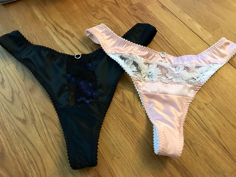 May include: Two pairs of satin lingerie with lace trim. One pair is black with black lace and the other is pink with white lace.