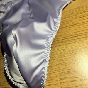 May include: A pair of light purple satin underwear with white lace trim.