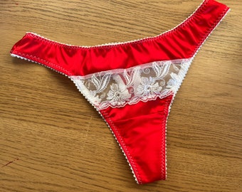 May include: Red satin lingerie with white lace trim. The lace has a floral design.