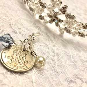 May include: A silver charm with a 1948 sixpence coin, a blue crystal bead, and a white pearl bead. The charm is attached to a silver chain.