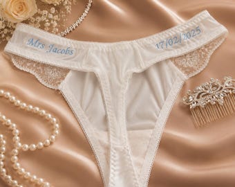 May include: White underwear featuring delicate lace side panels and light blue embroidery. The text "Mrs Jacobs" is stitched on the left side, and the date "17/02/2025" is embroidered on the right side of the waistband, creating a detailed design.