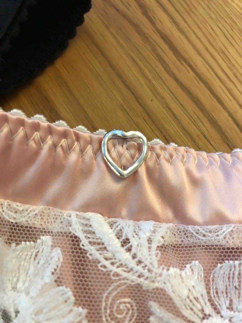 May include: A close-up of a pink satin and lace garment with a silver heart-shaped button.
