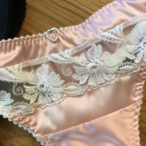 May include: Pink satin lingerie with white lace trim and a silver heart-shaped charm.