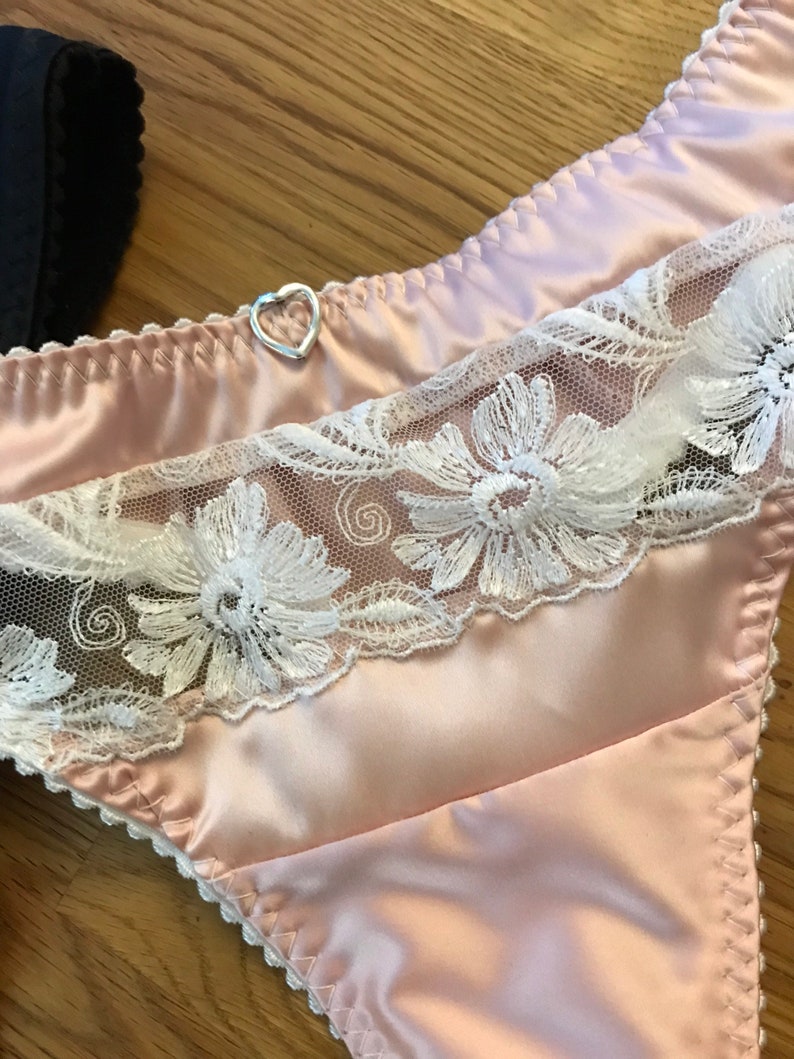 May include: Pink satin lingerie with white lace trim and a silver heart-shaped charm.