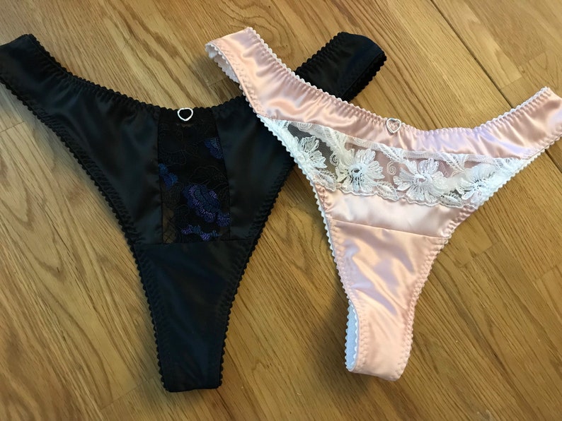 May include: Two pairs of satin thongs with lace trim. One thong is black with blue lace and the other is pink with white lace.