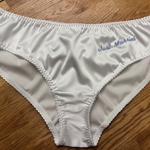 May include: White satin underwear with a blue embroidered message that says "Just Married".