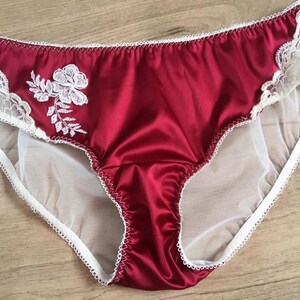 May include: Red satin underwear with white lace trim and a floral embroidery design.