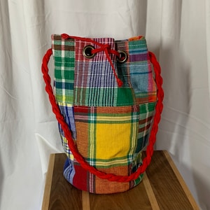May include: A colorful patchwork drawstring bag with a red cord. The bag is made of different plaid fabrics in shades of red, green, blue, yellow, and white.