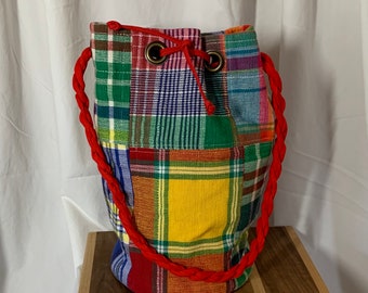 May include: A colorful patchwork drawstring bag with a red cord. The bag is made of different plaid fabrics in shades of red, green, blue, yellow, and white.