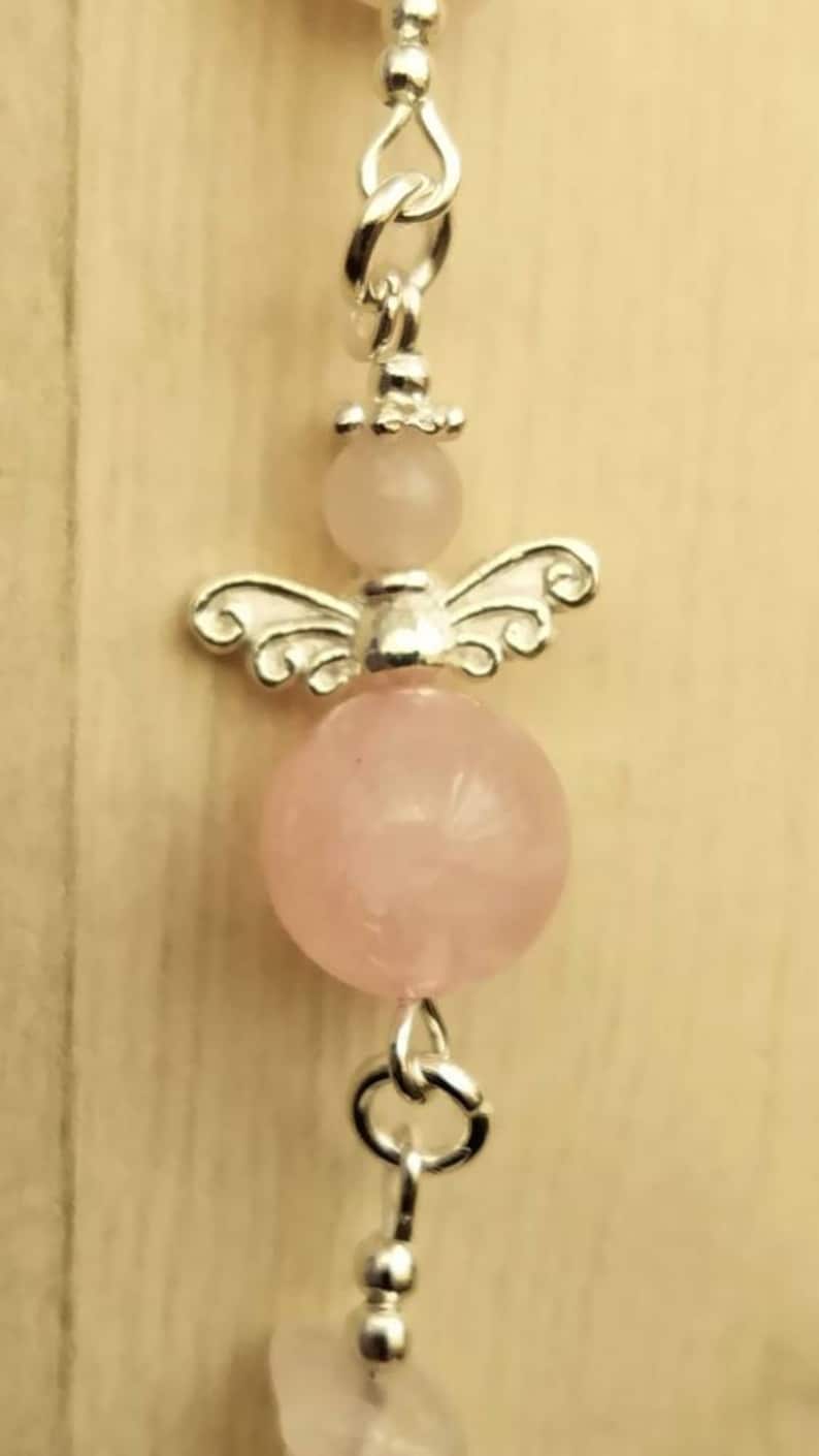 Puede incluir: Un brazalete de plata con una cuenta de cuarzo rosa y un dije de &aacute;ngel de plata.