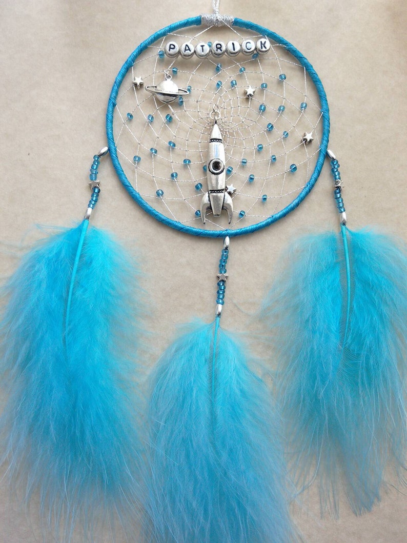 Pu&ograve; includere: Un acchiappasogni blu e argento con il nome "Patrick" scritto in perline argentate. L'acchiappasogni &egrave; decorato con un razzo, un pianeta e stelle. Ha tre lunghe piume blu che pendono dal basso.
