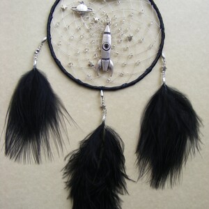 Pu&ograve; includere: Acchiappasogni nero con piume nere, perline argentate e un ciondolo a razzo argentato. L'acchiappasogni ha il nome "KYLE" scritto in perline argentate.