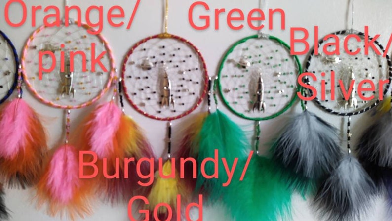 Pu&ograve; includere: Cinque acchiappasogni con cerchi e piume di diversi colori. I cerchi sono arancio/rosa, bordeaux/oro, verde, nero/argento e blu. Ogni acchiappasogni ha un ciondolo a forma di razzo argentato.