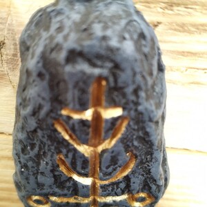 May include: A black stone with a gold symbol on it. The symbol is a stylized tree with a circle at the bottom.