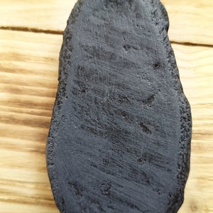 May include: A black, oval-shaped, smooth, and slightly textured piece of wood.