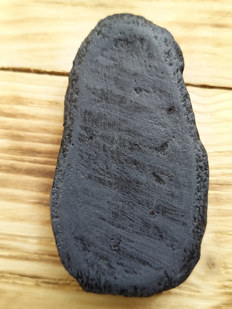 May include: A black, oval-shaped, smooth, and slightly textured piece of wood.