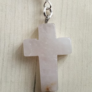 Puede incluir: Un colgante de cruz de cuarzo rosa rosa con una cadena de plata.