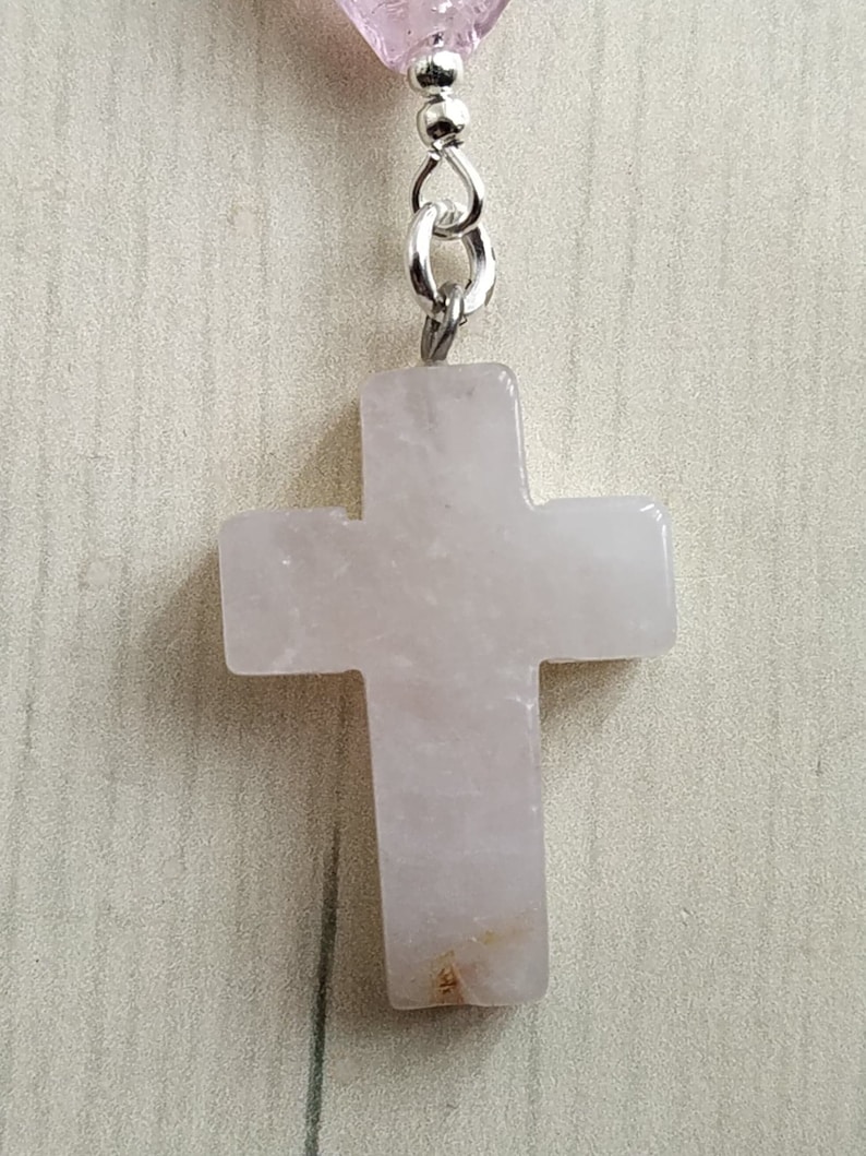 Puede incluir: Un colgante de cruz de cuarzo rosa rosa con una cadena de plata.