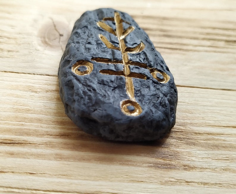 May include: A black stone with a gold tree symbol carved into it. The stone is smooth and has a textured surface.